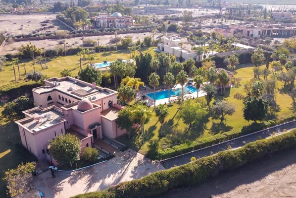 Vista aérea de um resort com vários edifícios, uma piscina e jardins bem cuidados.