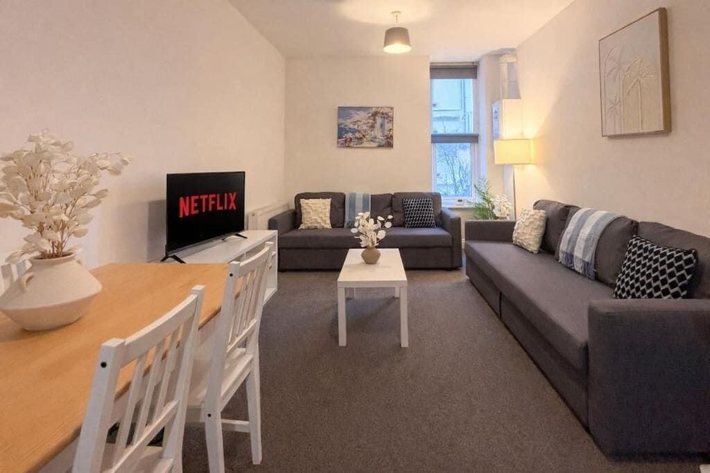 Una sala de estar moderna con un sofá, una mesa de centro y un televisor que muestra 'NETFLIX'.