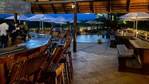 Un espace de restauration en plein air avec des tables et des chaises en bois, des parasols et un panneau affichant le menu.