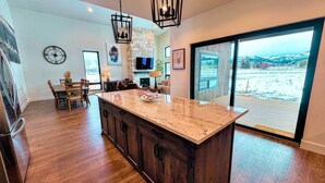 A spacious kitchen with a large island, wooden cabinets, and a stone fireplace. - Modern Family Retreat w/ Hot Tub, Teton Views, + A/C (Driggs)