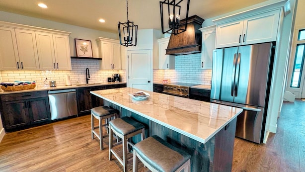 A modern kitchen with white cabinets, a large island with stools, stainless steel appliances, and a brick backsplash. - Modern Family Retreat w/ Hot Tub, Teton Views, + A/C (Driggs)