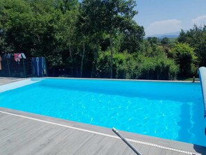 A rectangular swimming pool with clear blue water, surrounded by a wooden deck and a metal fence.