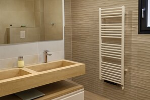 A bathroom with a wooden vanity, a mirror, a towel rack, and a textured wall.