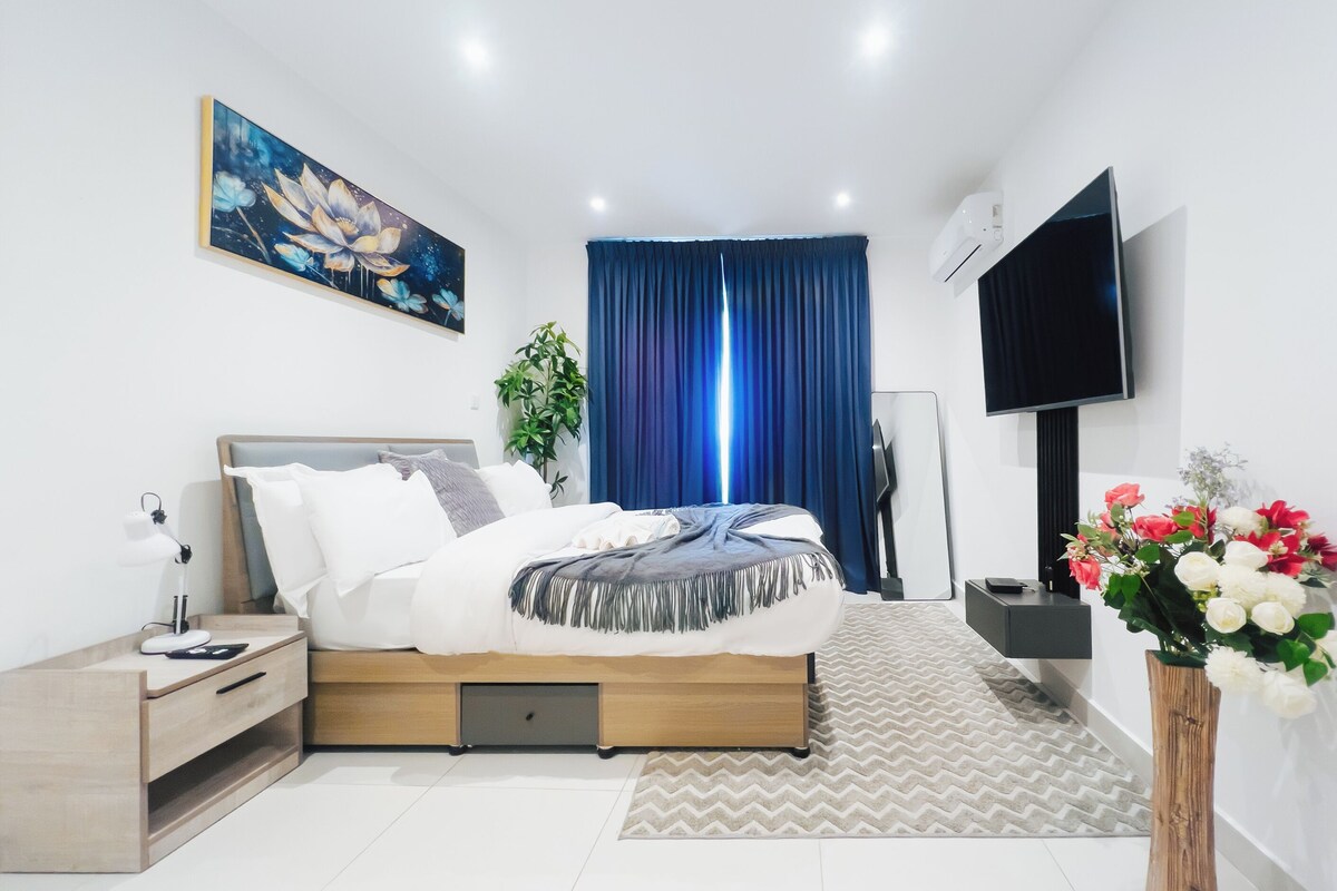 A modern bedroom with a bed, bedside table, TV, and a painting.