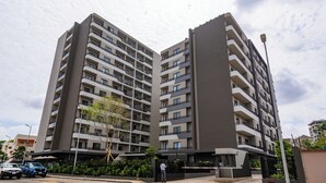 Un edificio residencial de varios pisos con balcones, una entrada protegida por un portón y vista a la calle.