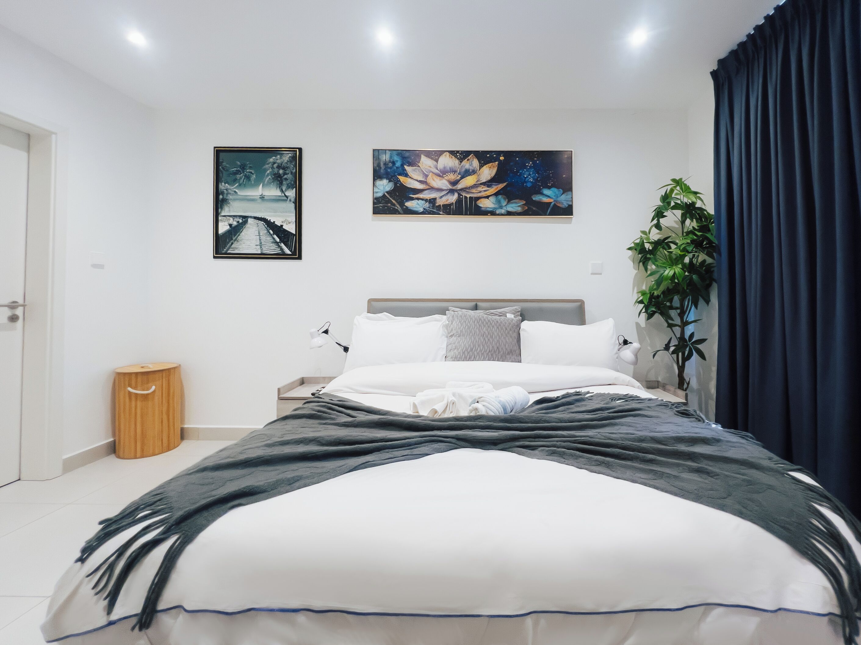 Een moderne slaapkamer met een bed, nachtkastje, lamp en een grote plant.