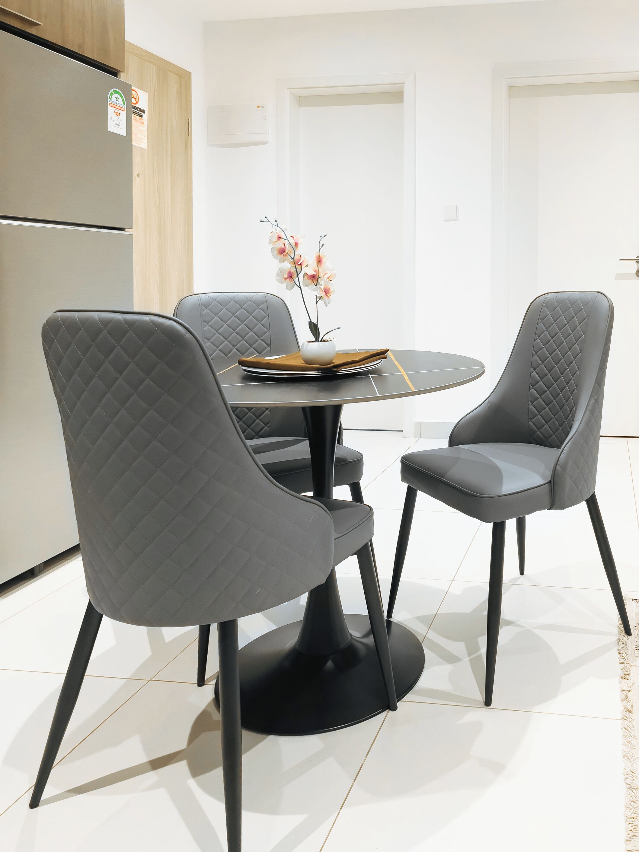A modern dining area with a round table, two chairs, and a vase with flowers.