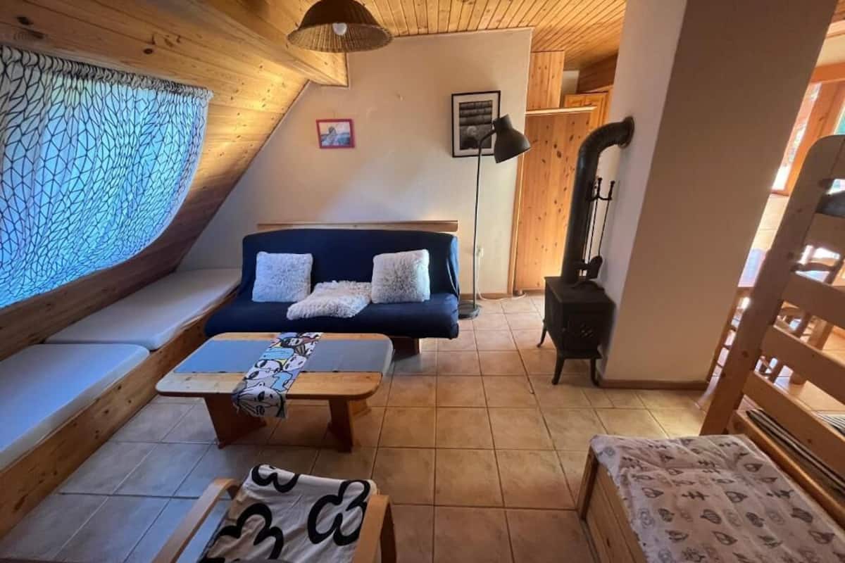 A cozy room with a sofa, a small table, and a bench. There is a fireplace and a window with a curtain.