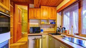 Una cocina compacta con armarios de madera, microondas, lavavajillas y ventana con persianas.