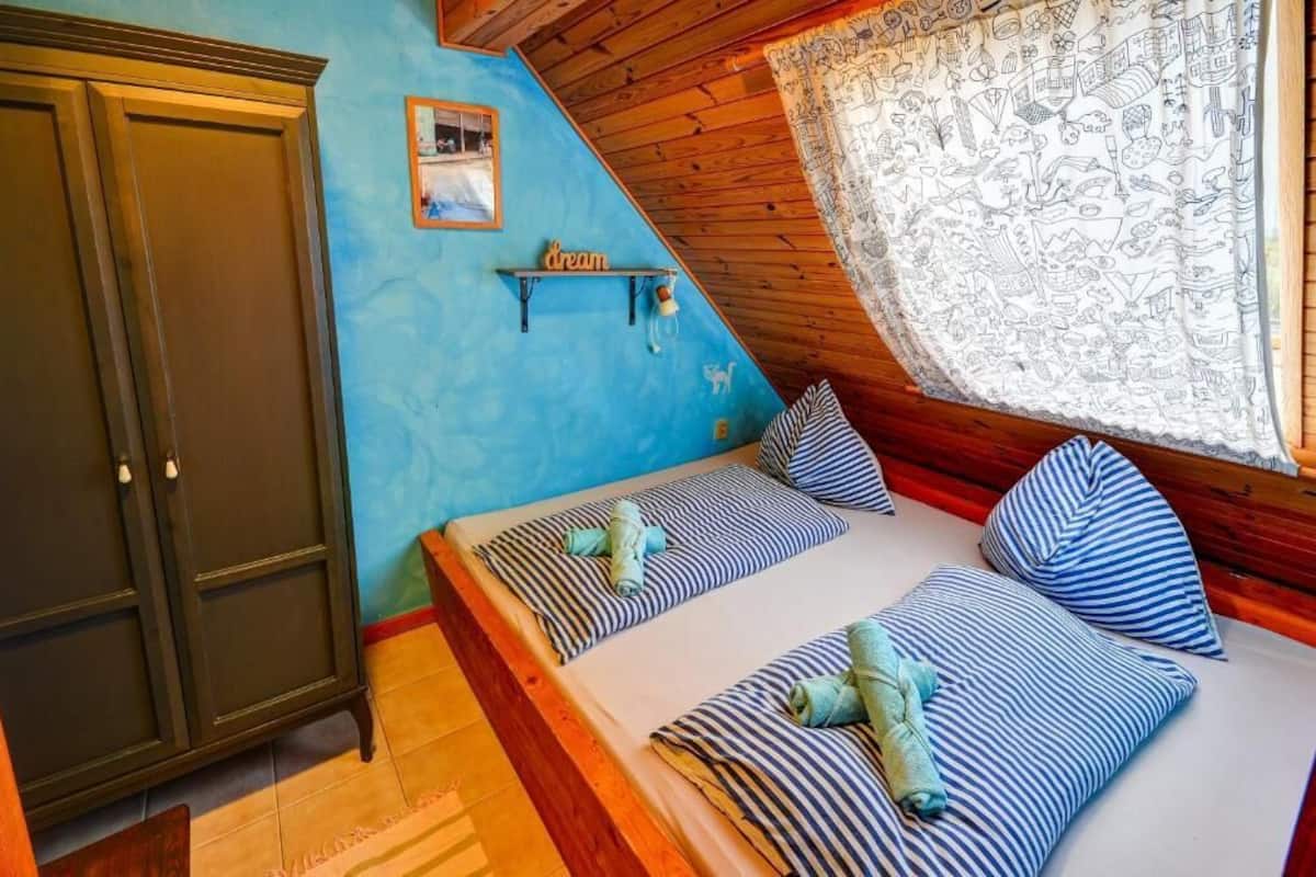 A bedroom with a sloped ceiling, a bed with striped bedding, a wooden wardrobe, and a wall-mounted shelf with a 'dream' sign.