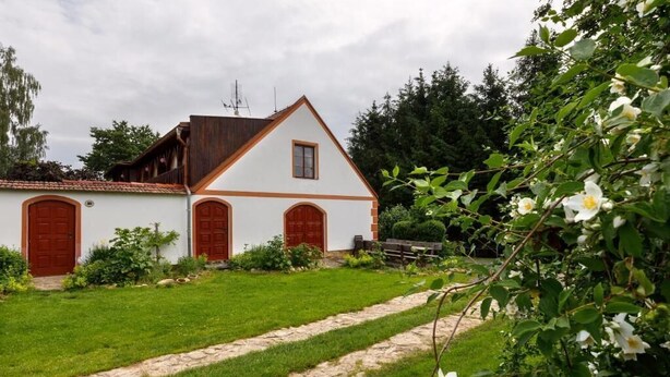 Un edificio blanco con techo inclinado y puertas rojas, rodeado de un césped cuidado y un sendero de piedra.