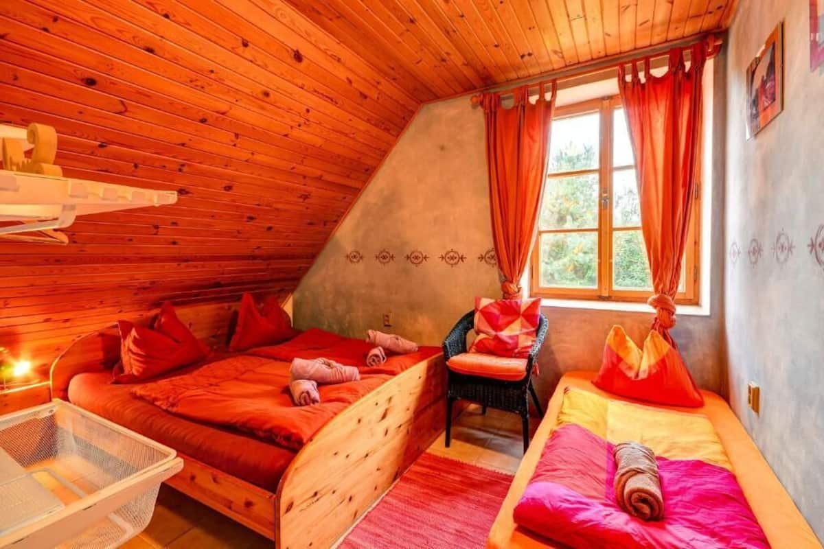 A cozy, wooden-paneled room with two beds, a chair, and a window with curtains.
