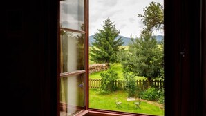 Una habitación con un ventanal amplio que ofrece vistas a un jardín cuidado, con valla de madera, césped y diversos árboles.