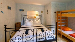 Una cama individual con estructura metálica negra, una cama litera de madera a la derecha y una mesita de noche con una lámpara.