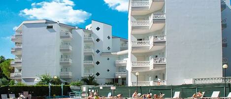 A swimming pool with lounge chairs and a building with multiple balconies.