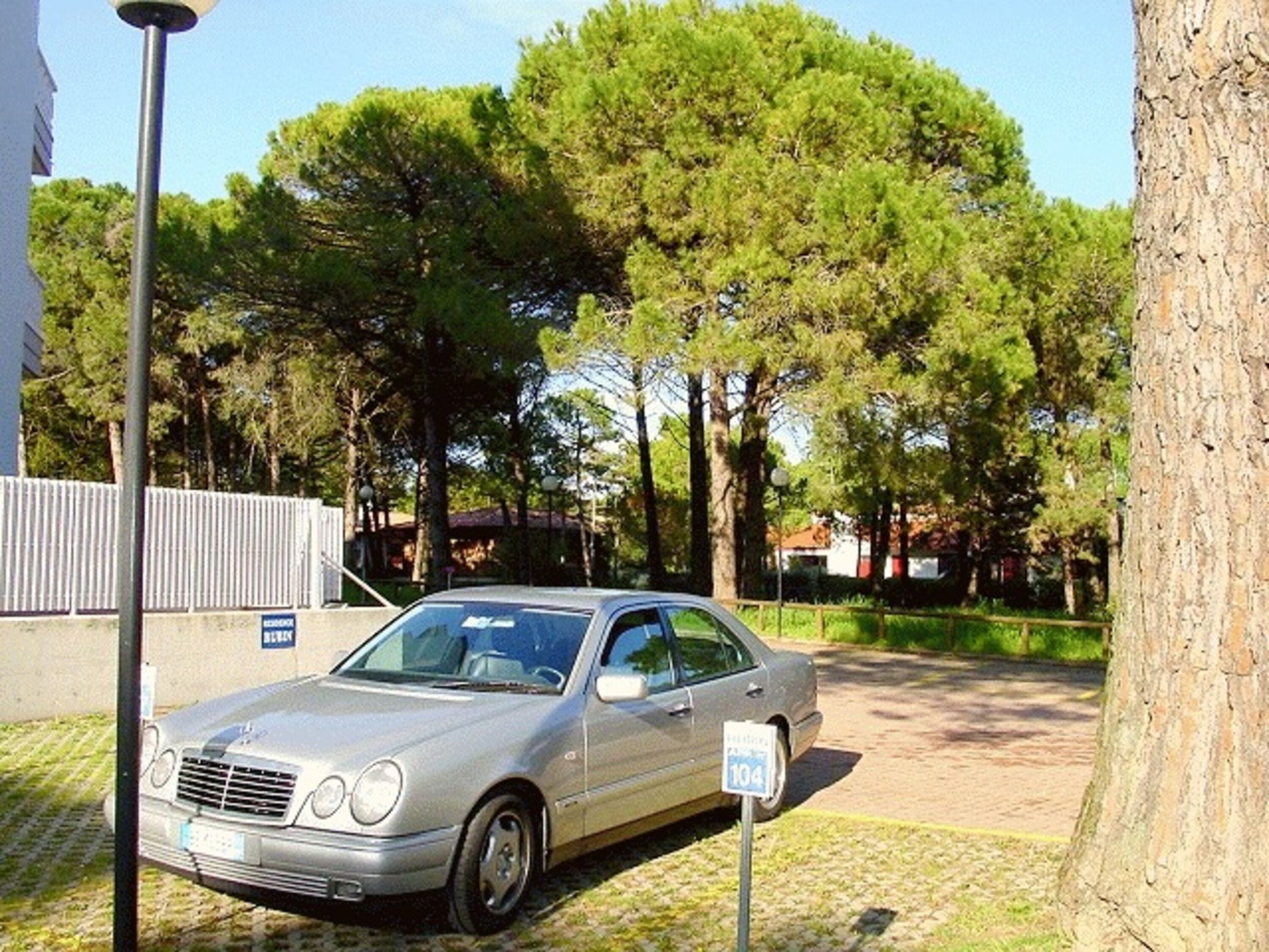 Un coche plateado estacionado en una calle empedrada con árboles al fondo.
