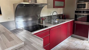 A modern kitchen with red cabinets, a stainless steel range hood, and a built-in microwave. - L écrin de l aube  (Grainville-la-Teinturière)