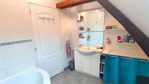 A bathroom with a bathtub, a sink, and a mirror. There are shelves with toiletries and a trash bin. - L écrin de l aube  (Grainville-la-Teinturière)