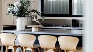 Una cocina moderna con una isla central, taburetes de bar, una campana extractora de acero inoxidable y un amplio ventanal.
