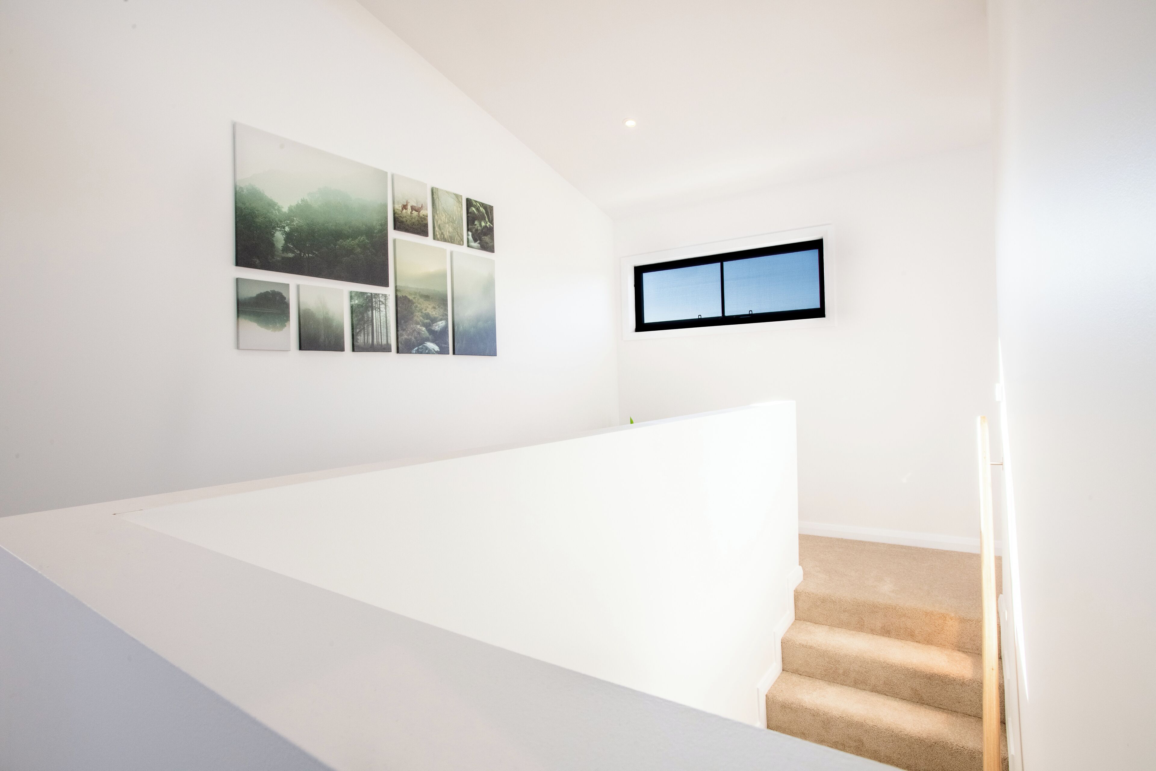 Un intérieur moderne avec un escalier blanc, une petite fenêtre et une série de tableaux encadrés accrochés au mur.