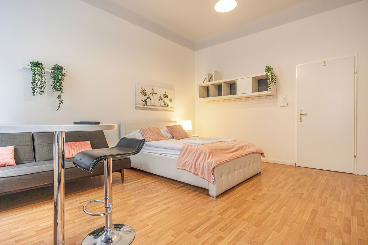 Ein modernes Schlafzimmer mit Bett, Sofa, Barhocker und Holzboden.