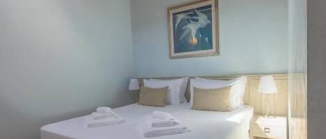 Quarto com teto de madeira, cama com roupa de cama branca, mesa de cabeceira e um quadro na parede.