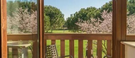 Un balcón con cubierta de madera, mobiliario exterior y vistas a árboles y césped.