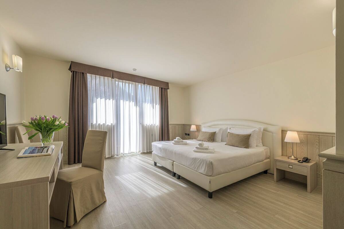 A hotel room with a bed, bedside tables, a desk, and a chair.