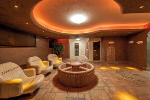Un'area benessere con poltrone rivestite di mosaici e una vasca idromassaggio centrale decorata a mosaico.