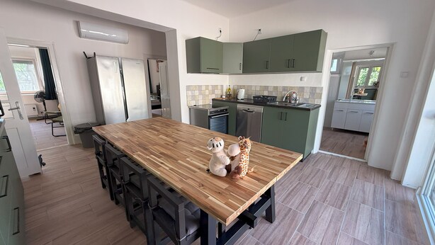 A modern kitchen with a wooden island, green cabinets, and a dining area.