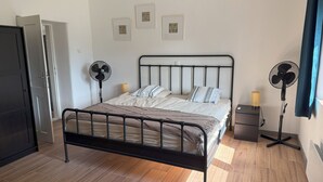 A bedroom with a bed, two wall-mounted fans, a small bedside table, and a door.