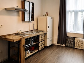 A compact kitchen with a wooden countertop, a built-in oven, a refrigerator, and a window with curtains.