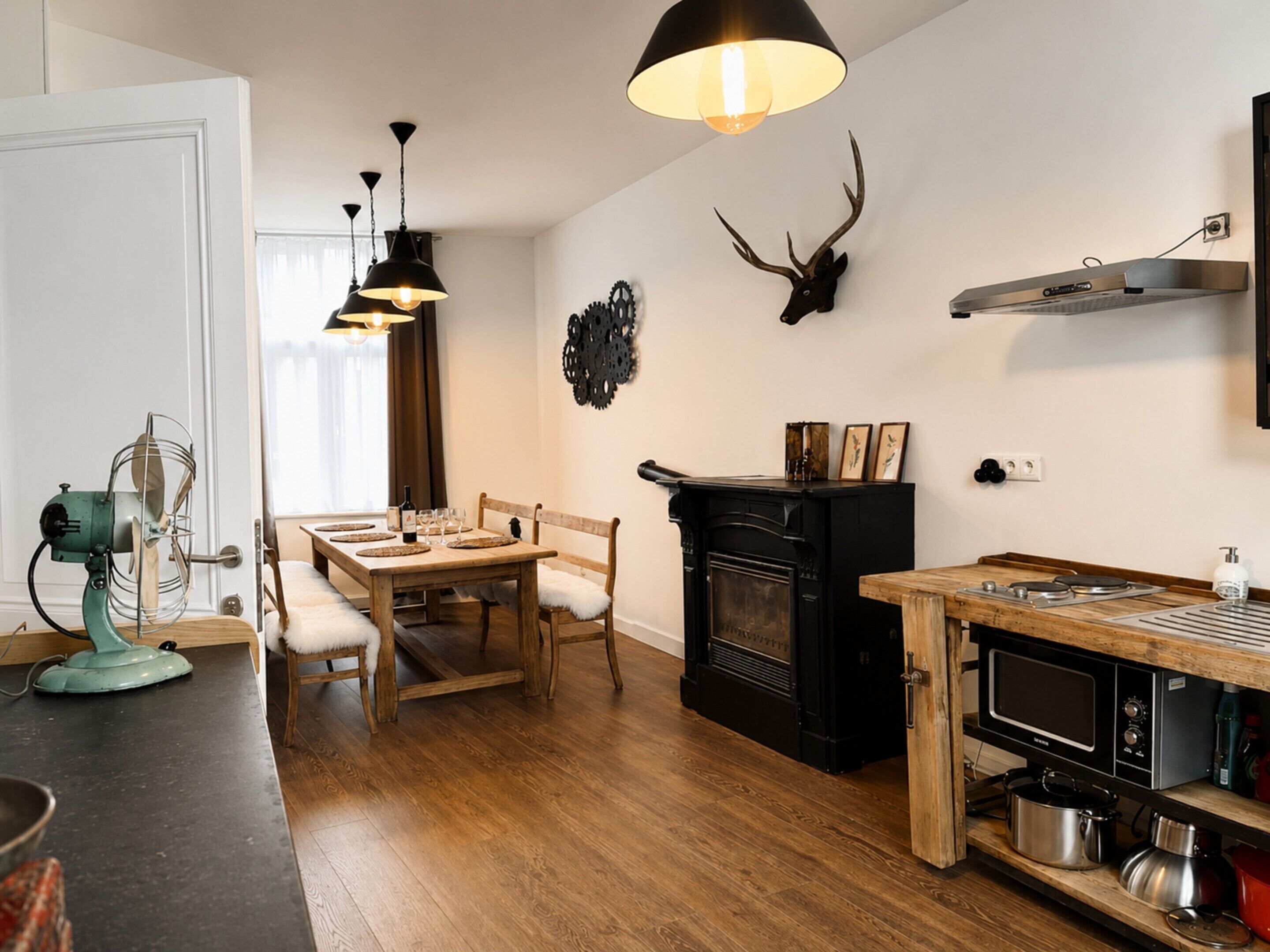 Una cucina moderna con zona pranzo, pavimento in legno, camino e testa di cervo appesa al muro.