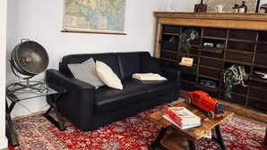A living room with a black sofa, a wooden coffee table, a map on the wall, and a bookshelf. - Chic Vintage Apartment in Spa (Spa)