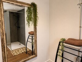 Un baño con un espejo grande, una ducha, un perchero y un taburete pequeño.