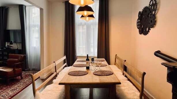 A dining area with a wooden table, cushioned chairs, and a chandelier. - Chic Vintage Apartment in Spa (Spa)