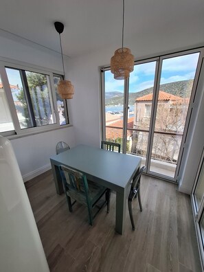 Un espace repas comprenant une table et des chaises, de grandes fenêtres et une vue sur des bâtiments et des collines.