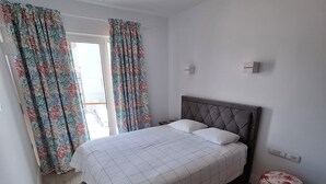 Ein Schlafzimmer mit einem Bett, Vorhängen, einem Nachttisch und einem runden Pouf.