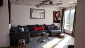 Een moderne woonkamer met een donkergrijze bank, een ronde salontafel en een groot raam met gordijnen.