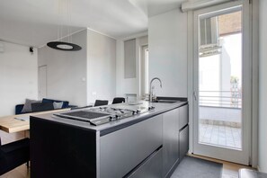 A modern kitchen with a central island, a dining area with a table and chairs, and a sliding glass door to an outdoor balcony. - Hostmate - Milano - Muratori - Porta Romana  (Milano)