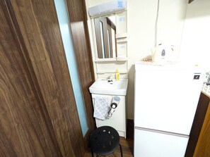 Ein kleines Badezimmer mit Holztür, einem weißen Waschbecken mit Handtuch und einem kleinen schwarzen Hocker.