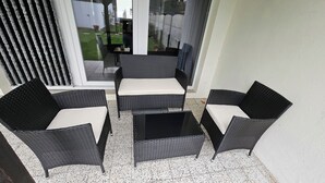 Un petit espace patio aménagé avec des meubles en osier et une porte vitrée donnant sur un jardin.
