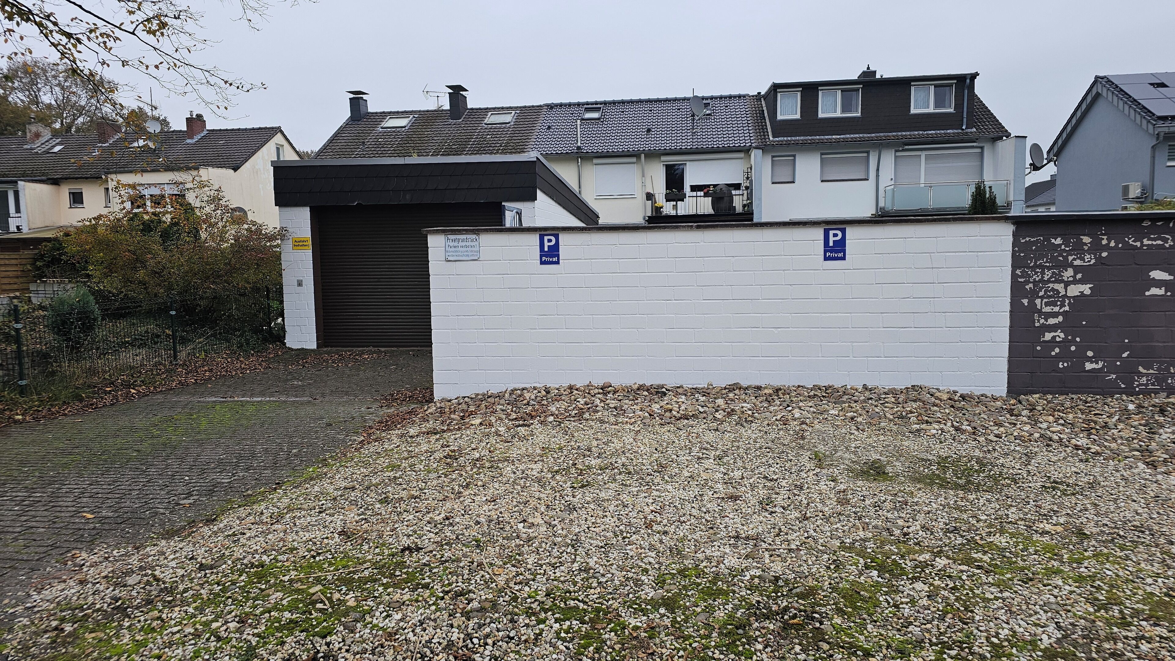 Ein Wohngebiet mit einer weißen Mauer, einer Schotterauffahrt und einer Garagentür.