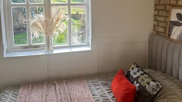 A room with a window, a bed with patterned bedding, a red pillow, and a framed picture on the wall.