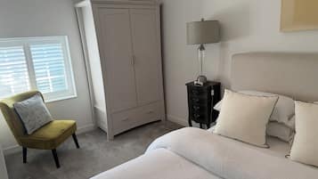 Una camera da letto con un letto, una sedia, un armadio, un comodino con una lampada e una finestra con persiane.