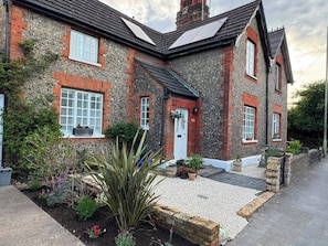 A stone house with a white door, windows with shutters, and a gravel driveway.