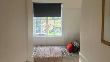 Ein schmales Zimmer mit Fenster, einer Sitzbank und einer Tür.