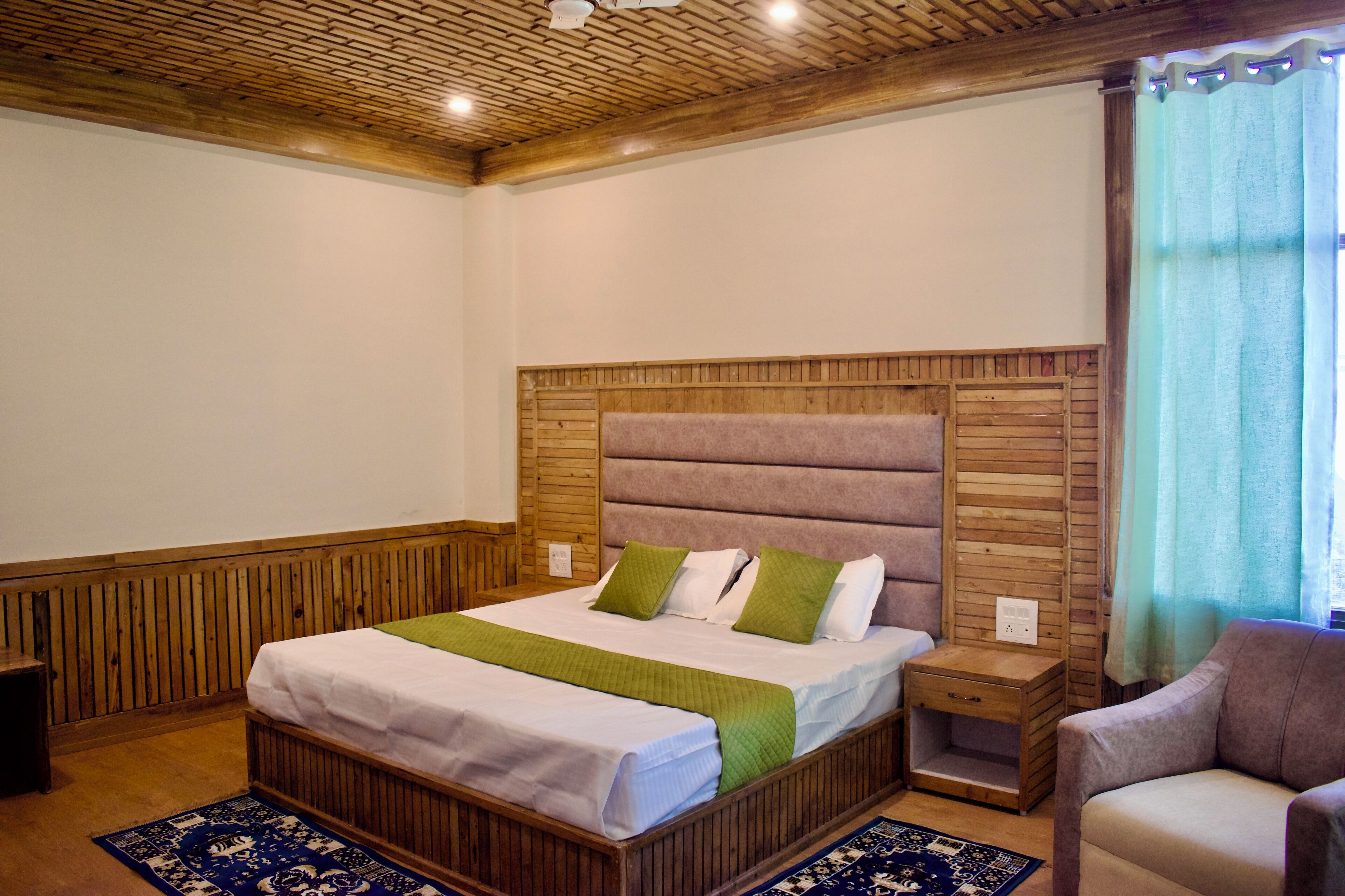 Un dormitorio con estructura de cama de madera, mesita de noche, una silla y alfombra estampada.