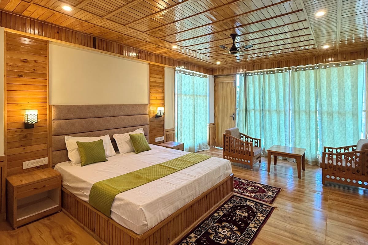 A wooden-paneled bedroom with a large bed, bedside tables, a nightstand, a wooden chair, a small table, and a window with curtains.