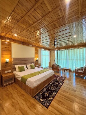 Camera da letto con pannelli in legno, un letto grande, comodini, un tavolino da notte, una sedia di legno, un piccolo tavolo e una finestra con tende.